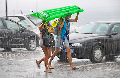 A couple is walking through heavy rain trying to protect themselves with an inflatable air mattress
