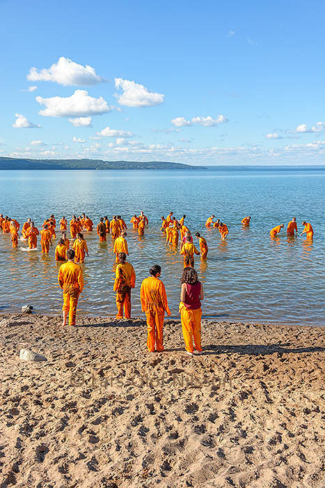 A number of people dressed in orange are wading out into a lake