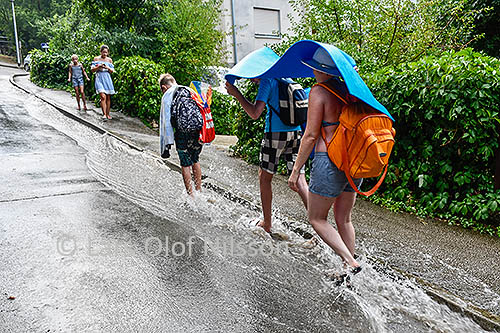 A family is walking in a gutter covering themselves against a heavy rain