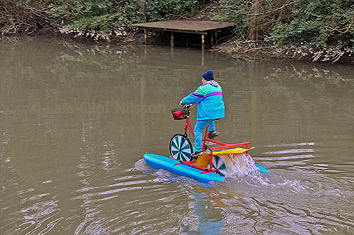 A man is cycling on a river wearing sensible weatherproof clothing