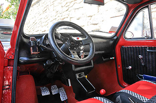 Interior of a red Fiat 500 with steering wheel,  dashboard and pedals visible