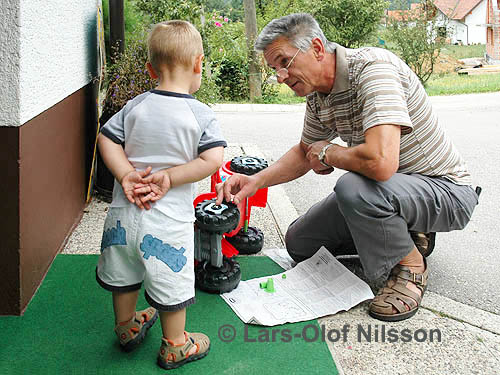 A grandfather is helping his grandson with a toy car