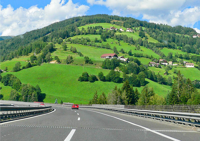 Just a couple of cars on the Autobahn in Austria with some farm buildings on a hill in the background