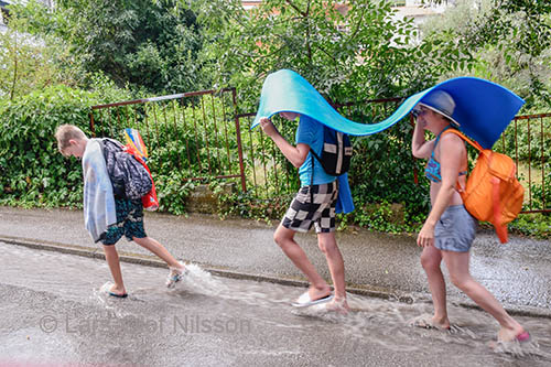 A family is walking in the gutter with sleeping mats over their heads to protect them from heavy rain.The image illustrates the idiom 'follow the leader' as a reminder to be careful when you use idioms.