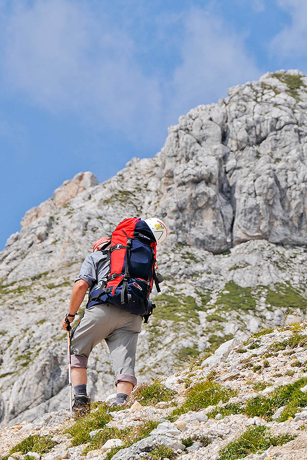 A man wearing a large rucksack is hiking in the mountains. The image illustrates the idea of insuring gear before doing something adventurous.