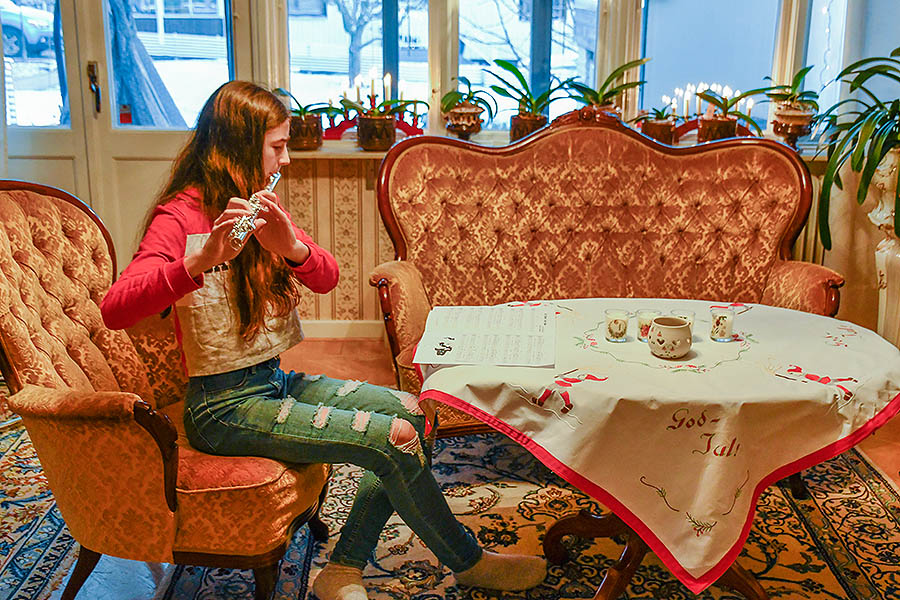 A young girl is practising playing the flute in a living-room. The purpose of the image is to illustrate the difference between practice and practise.