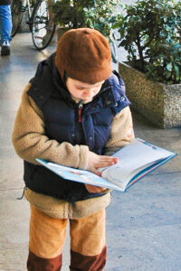 A small boy is reading a book while walking on a pavement. The image is meant to illustrate the concept of a critic.