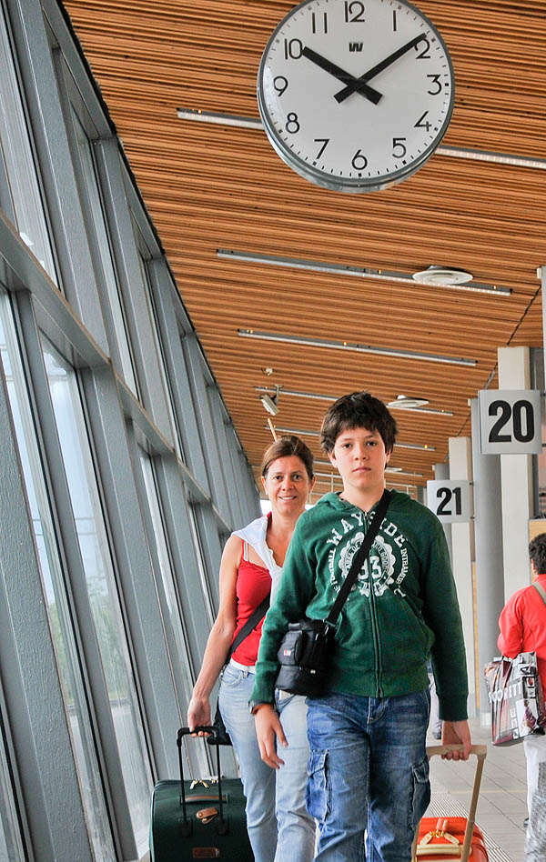 A woman and her son in a railway station. A clock above them shows nine minutes past ten. The word minute is a measure of time, but it can also mean very small.