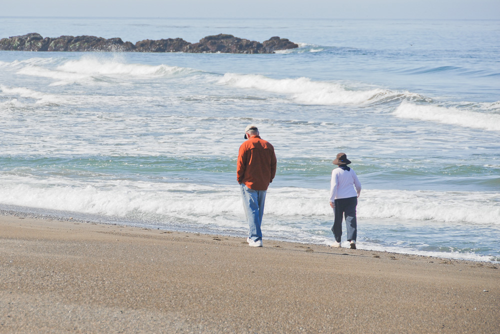 A man and a woman are walking along a beach. The image illustrates the word husband.